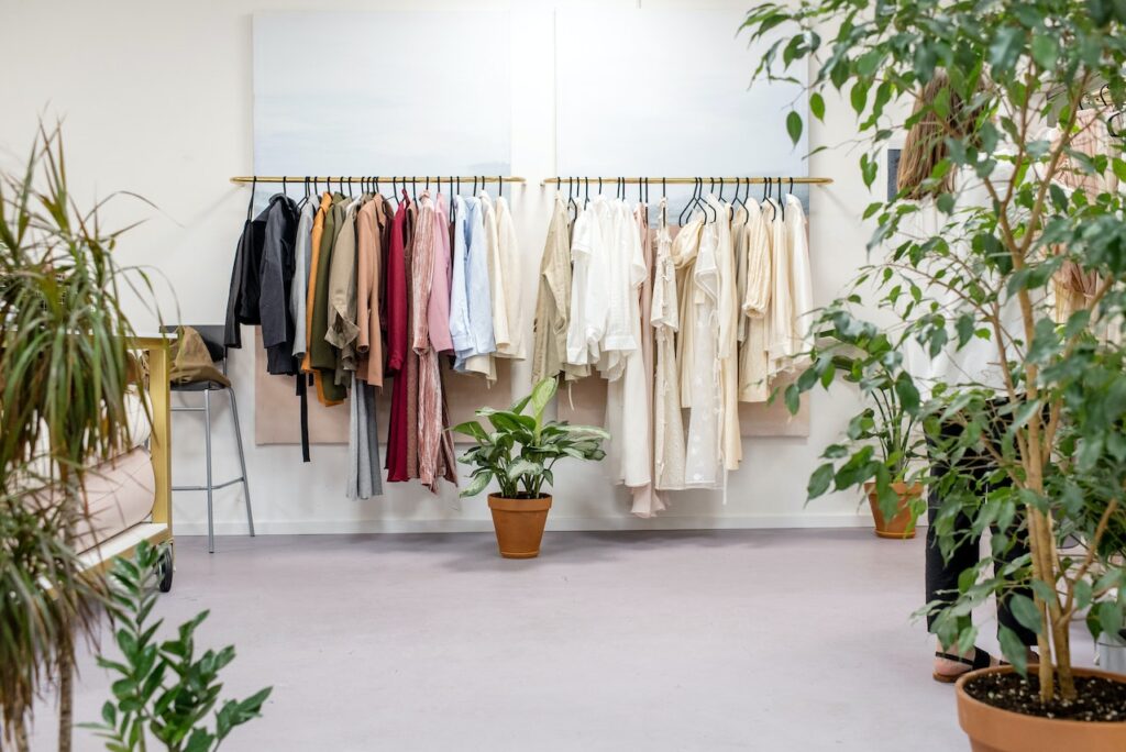 Clothing on a rack in a well-lit room, with plants in the foreground